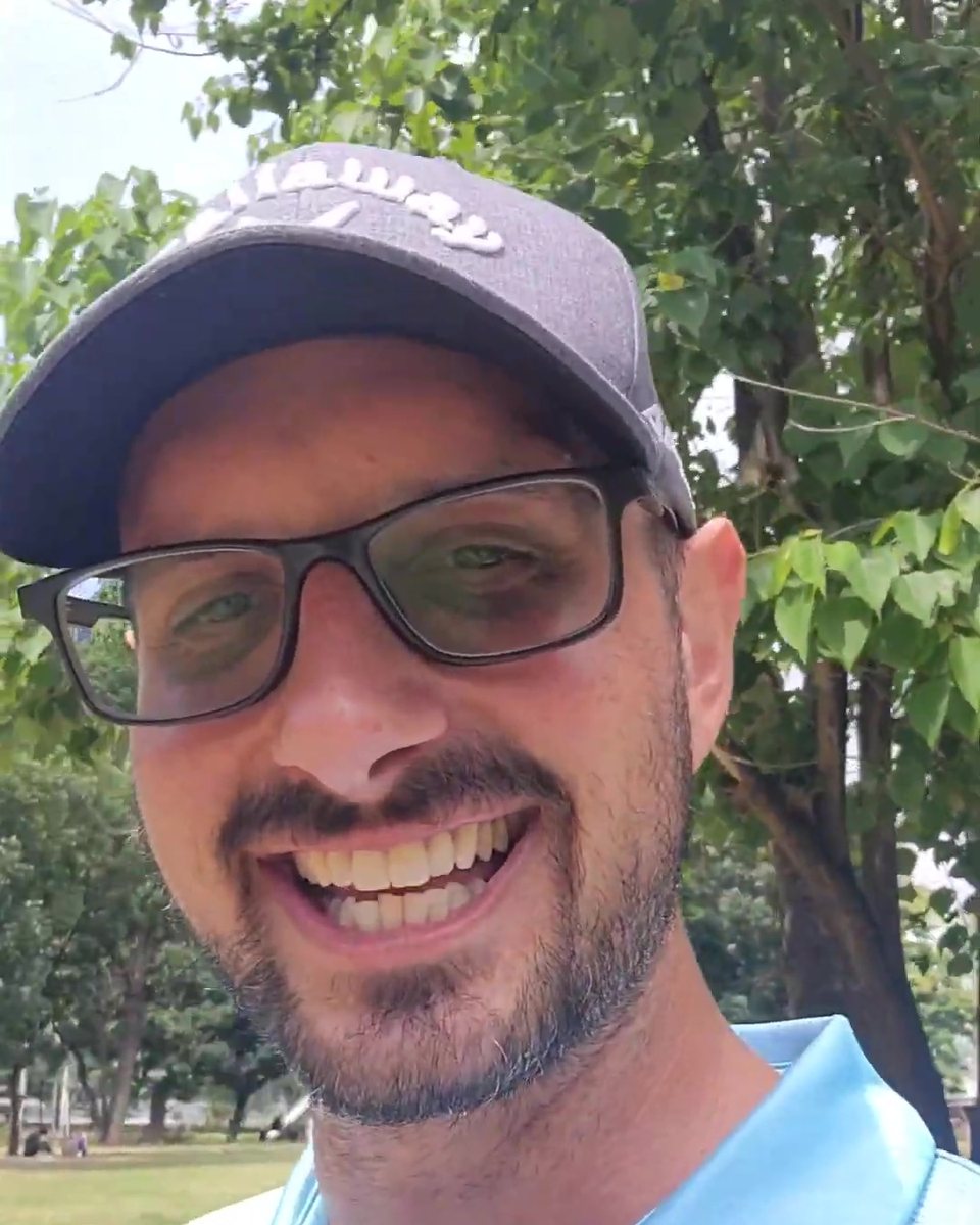 Todd Michael Gori smiling in a park, wearing a navy cap, glasses and a light blue polo