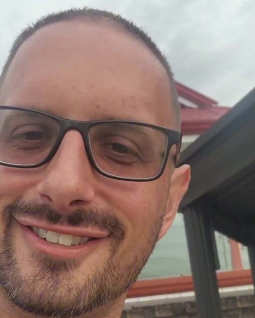 Todd Michael Gori smiling outdoors, wearing glasses and a navy polo shirt